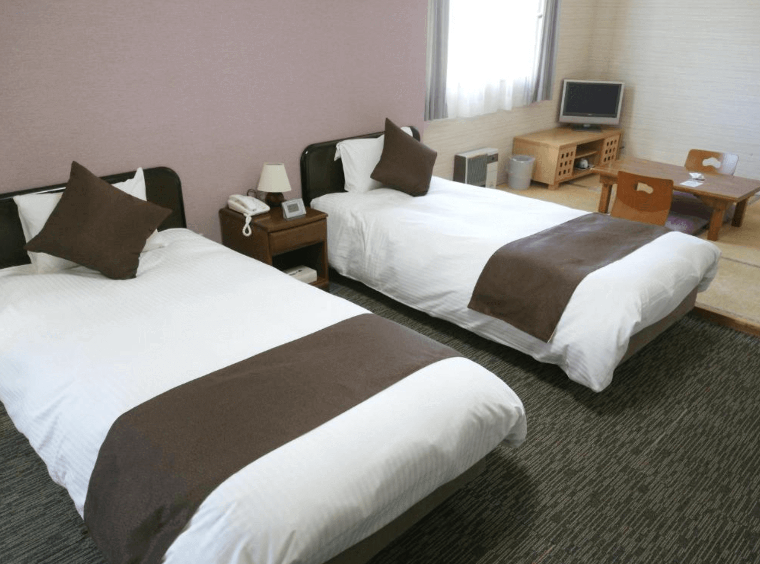 【富良野住宿】北國度假飯店 (Resort Inn North Country) 客房，兩張單人床鋪設白色床單與棕色抱枕，窗邊擺放小電視與矮桌椅，簡約舒適。