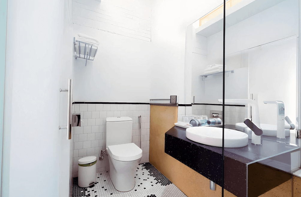 【高雄中央公園住宿】同．居 With Inn Hostel浴室：簡潔現代的衛浴空間，設有白色洗手台、大面鏡子與乾濕分離淋浴間，搭配黑白小花磚地板。