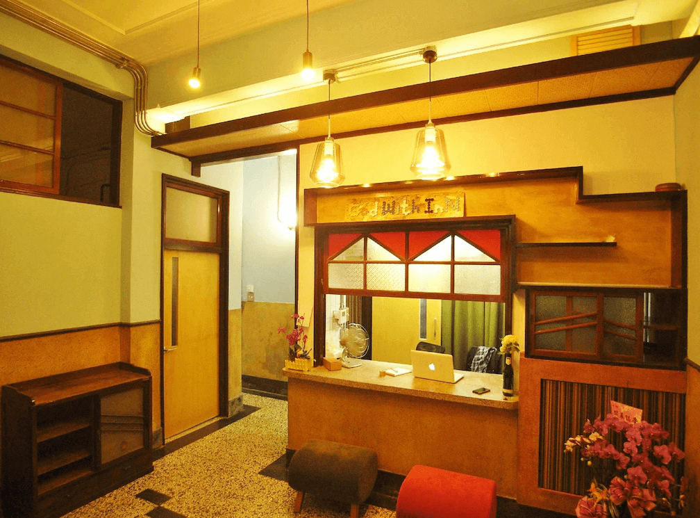 【高雄中央公園住宿】同．居 With Inn Hostel大廳：復古風格接待櫃檯，木質與磨石子地板設計，溫暖燈光搭配懷舊元素，營造親切的住宿氛圍。