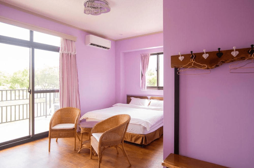 【玉里住宿】「吾笠塢民宿」溫馨紫色雙人房，房內設有大床、藤椅與玻璃桌，落地窗外可見自然綠意景色。