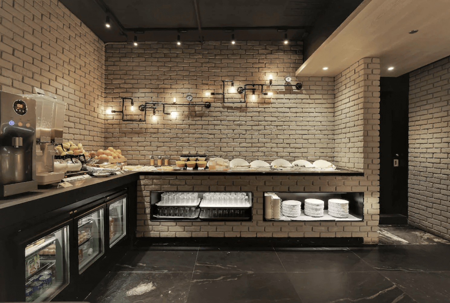 【前金住宿】高雄喜達絲飯店 — 自助餐區：磚牆工業風格餐廳，自助吧檯提供各式麵包、飲品與餐具，氛圍溫馨又具設計感。