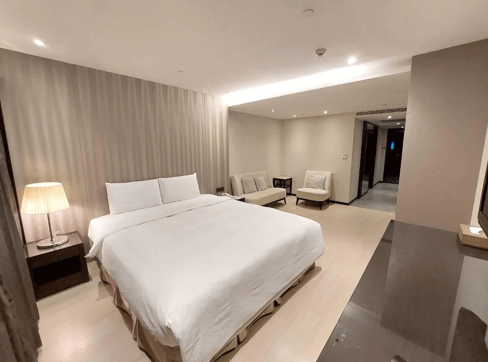 【高雄中央公園住宿】塔木德酒店高雄愛河館客房：典雅雙人房型，配有舒適大床、柔和燈光與沙發休憩區，氛圍溫馨安靜。