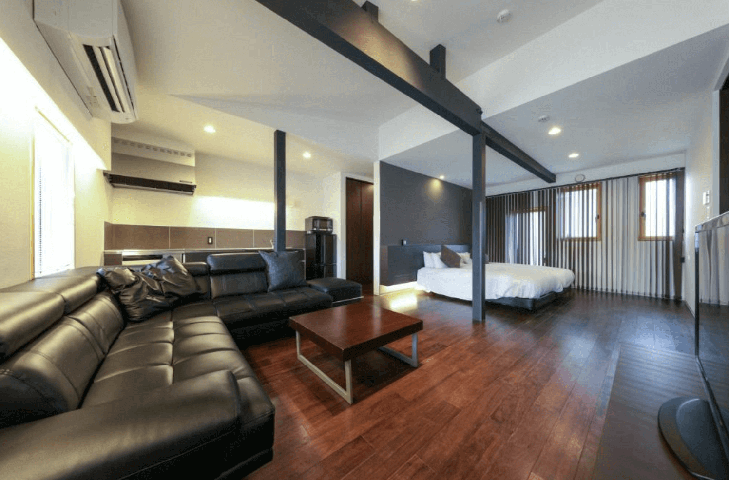 【富良野住宿】富良野Natulux飯店 (Furano Natulux Hotel) 豪華家庭房，木地板搭配現代黑色皮沙發與咖啡桌，開放式格局結合床鋪與廚房區，舒適大方。