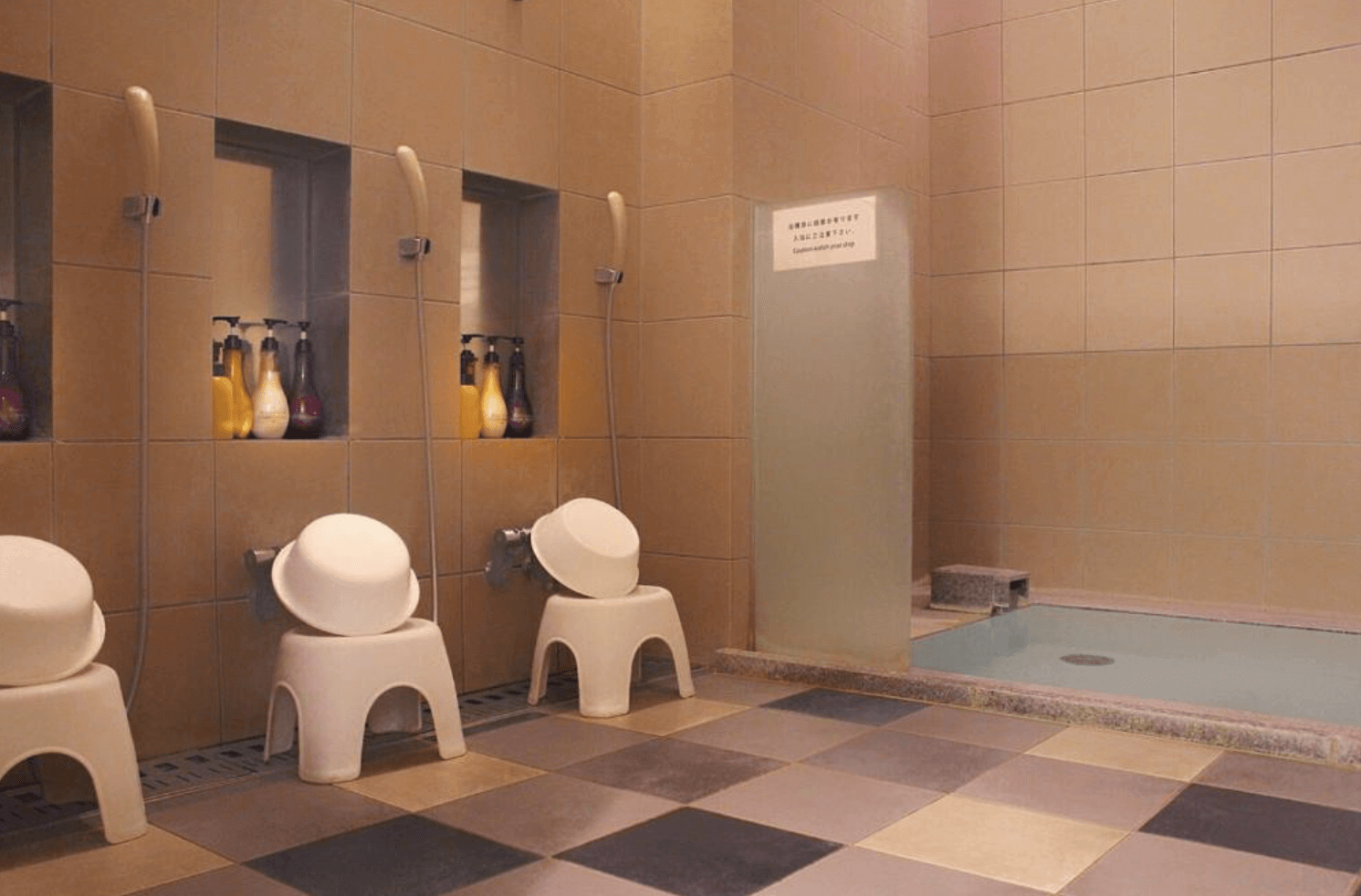 【富良野住宿】富良野Natulux飯店 (Furano Natulux Hotel) 公共浴場盥洗區，設有多個沖洗座位、盥洗用品與旁邊的泡湯池，環境整潔寬敞。