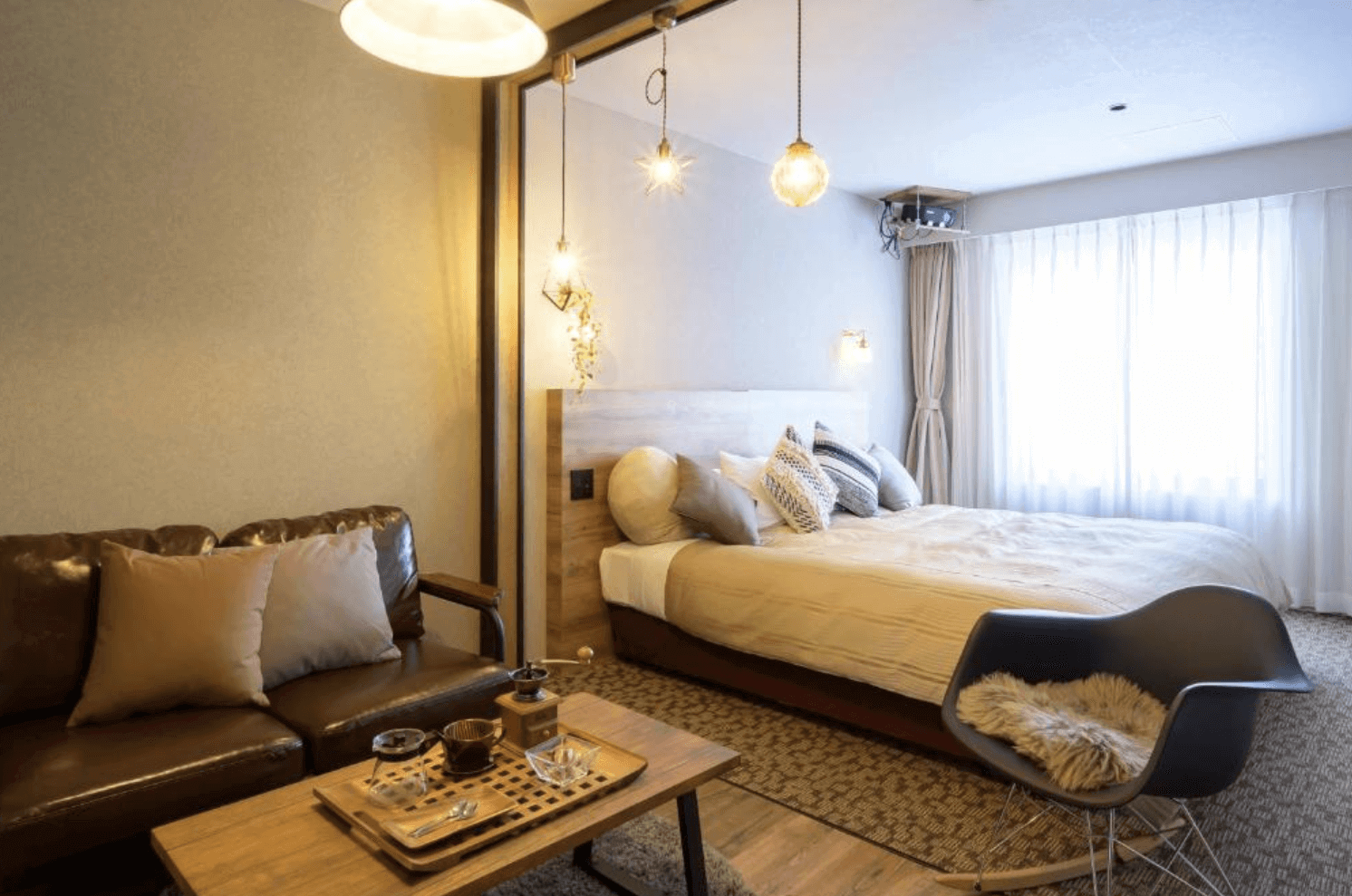 【富良野住宿】富良野度假飯店Edel Warme (Hotel Edel Warme) 客房，設有雙人床與皮沙發，吊燈與抱枕點綴溫馨氛圍，大窗戶引入自然光線。