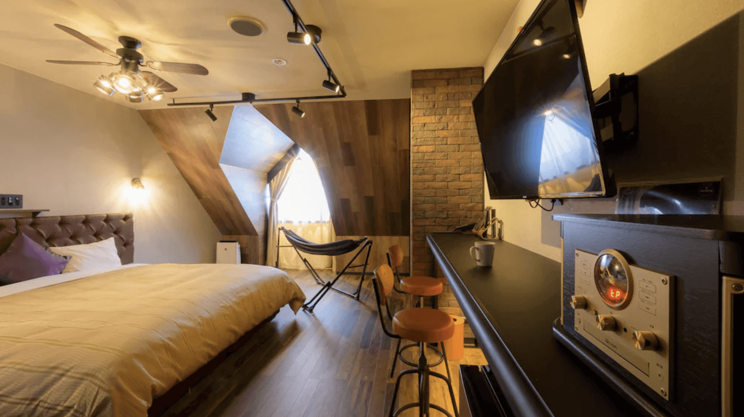 【富良野住宿】富良野度假飯店Edel Warme (Hotel Edel Warme) 客房，特色斜頂設計與木質牆面，配置雙人床、吧檯座椅、大電視與吊扇燈，風格現代又溫暖。