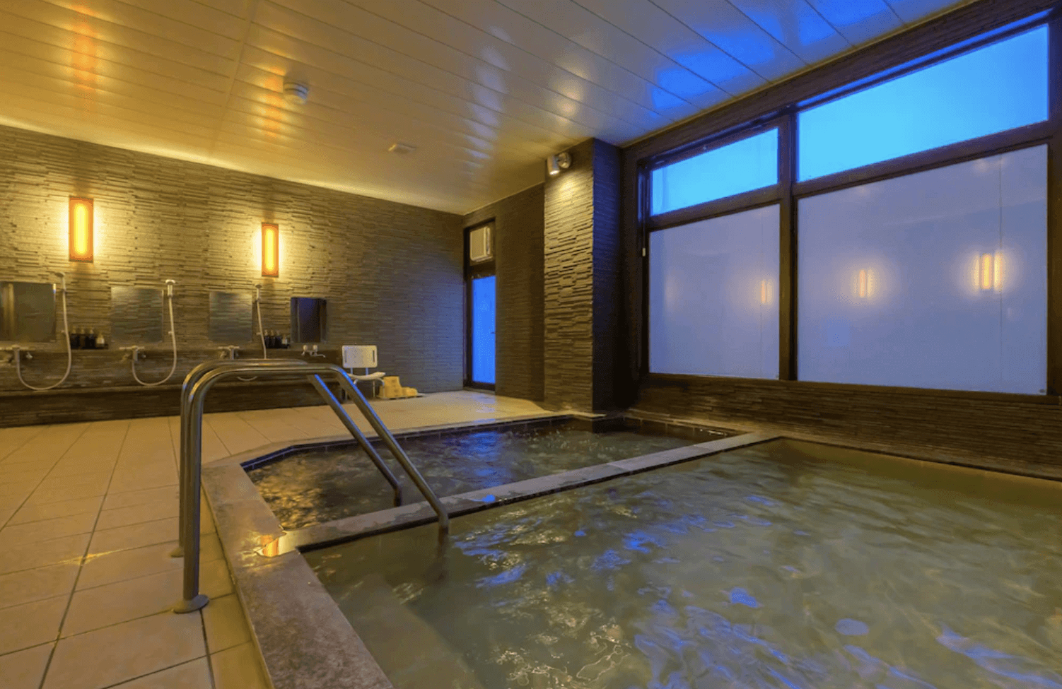 【富良野住宿】富良野度假飯店Edel Warme (Hotel Edel Warme) 室內溫泉浴場，設有沖洗區與寬敞溫泉池，昏黃燈光營造放鬆氛圍。