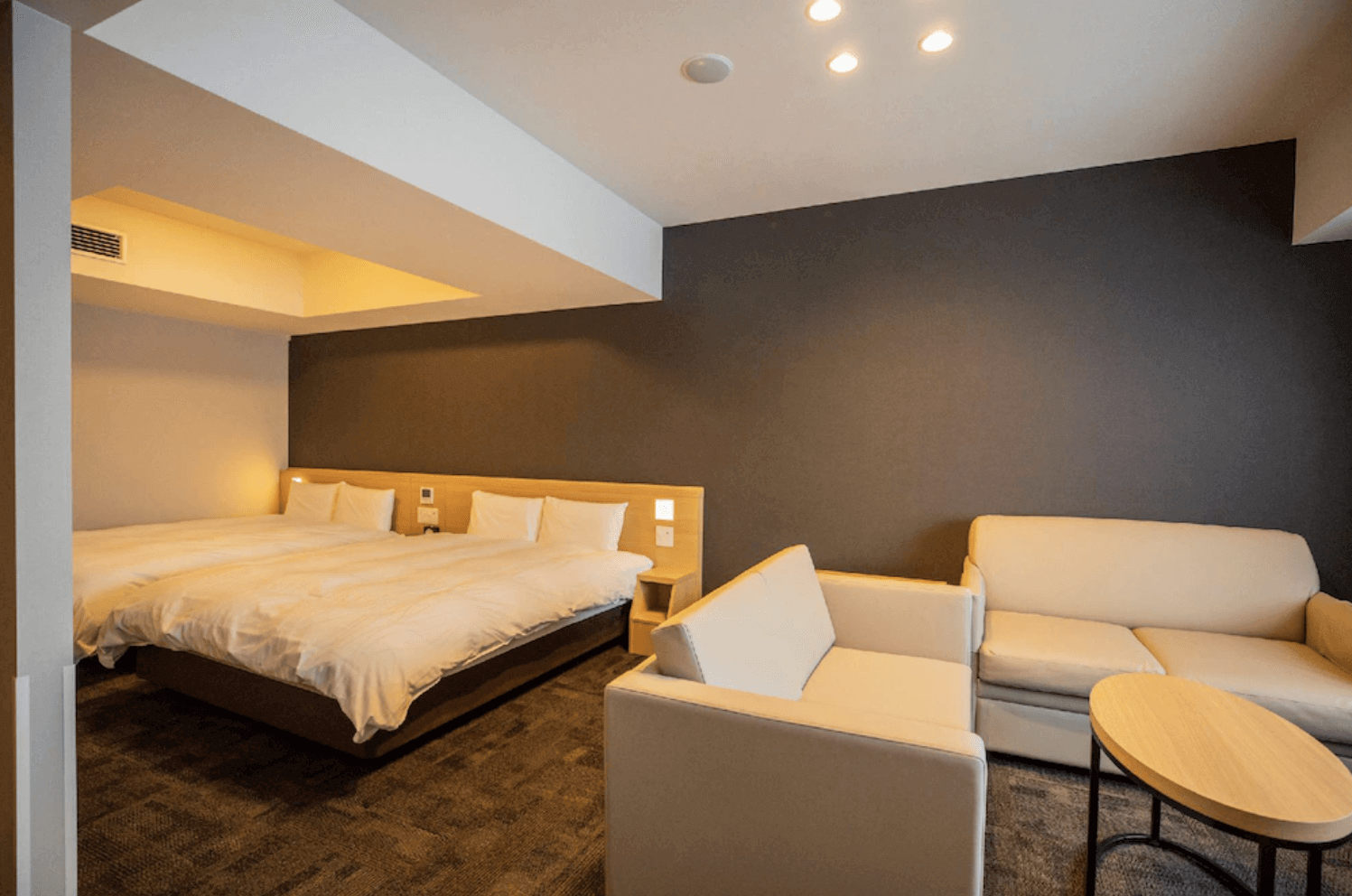 【富良野住宿】富良野拉維斯塔溫泉酒店 (La Vista Furano Hills Natural Hot Spring) 家庭房，配置兩張雙人床與米色沙發組及圓形茶几，房間寬敞舒適，氛圍溫暖雅致。