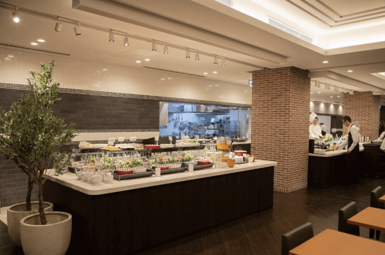 【富良野住宿】富良野拉維斯塔溫泉酒店 (La Vista Furano Hills Natural Hot Spring) 餐廳自助早餐區，擺放豐盛的沙拉、甜點與各式料理，開放式廚房內廚師正在準備餐點，環境明亮現代。