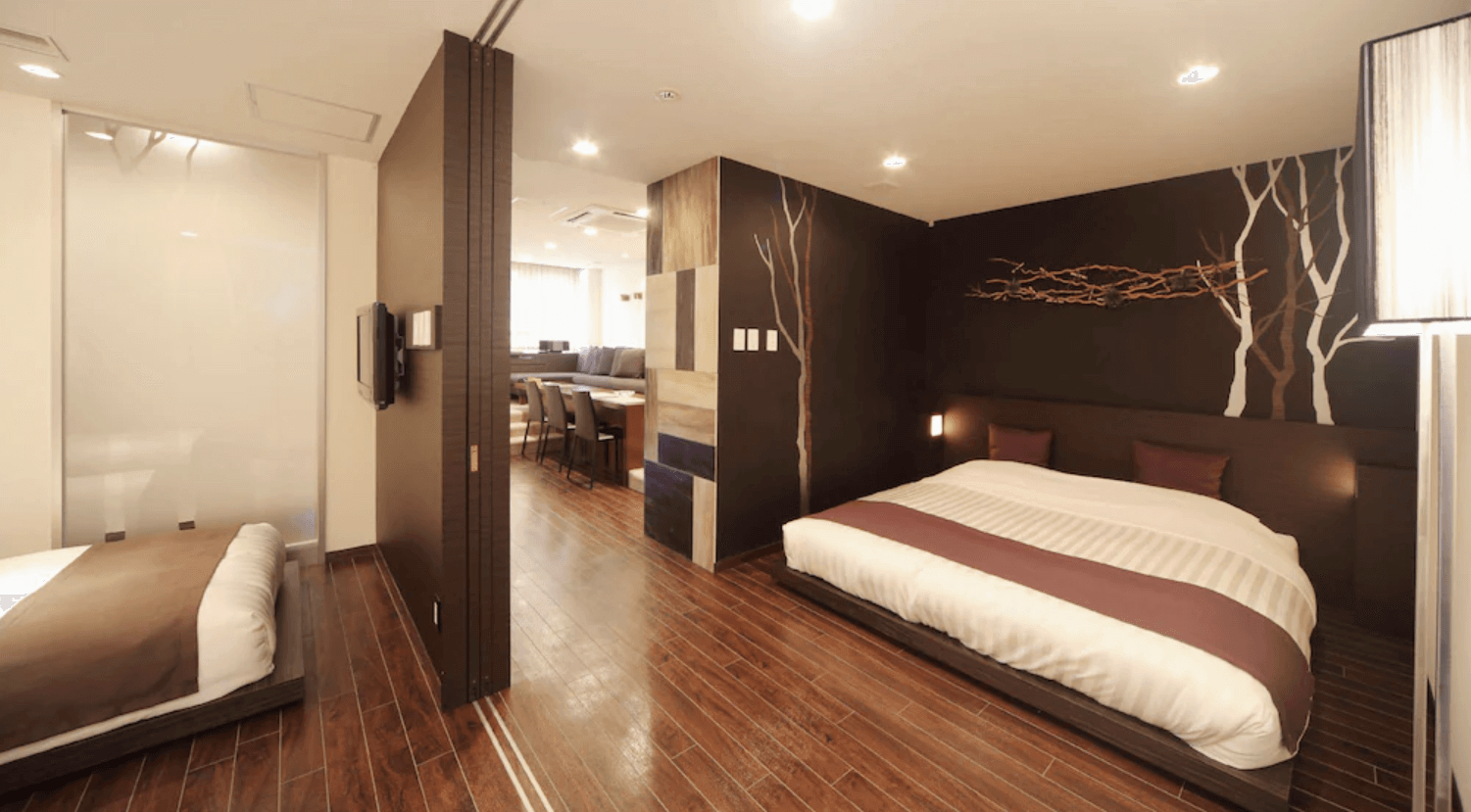 【富良野住宿】富良野自然森林飯店 (Hotel Naturwald Furano) 客房一景，深色木地板搭配樹木壁畫設計，設有雙人床與分隔式空間，營造自然雅緻氛圍。