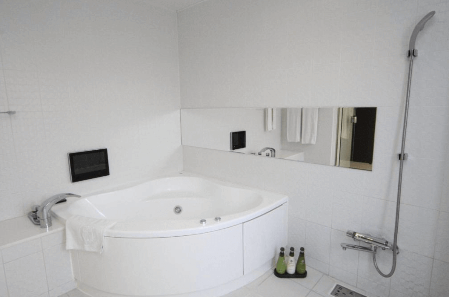 【富良野住宿】富良野自然森林飯店 (Hotel Naturwald Furano) 浴室，設有圓弧形按摩浴缸與淋浴設備，純白設計搭配大片鏡面，乾淨明亮。