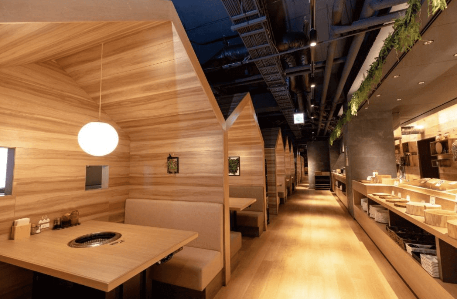 【富良野住宿】富良野自然森林飯店 (Hotel Naturwald Furano) 餐廳內部設計，木質包廂式座位搭配燒烤爐桌面，空間溫暖舒適，走道一旁擺放各式自助餐料理。