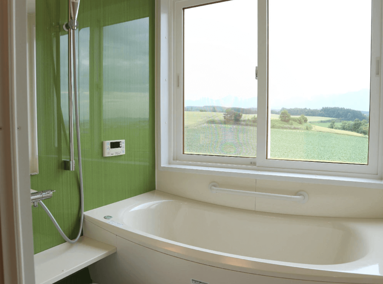 【富良野住宿】富良野風景民宿浴室：設有浴缸與淋浴設備，浴室窗外能看到綠意盎然的農村景致。