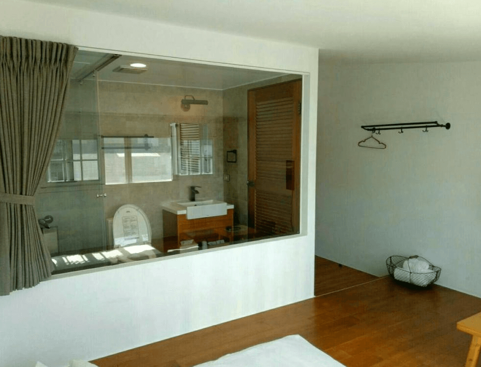 【玉里住宿】「小時公館城西」房內設計，床邊設有大片玻璃窗隔間可見浴室空間，衛浴設備現代簡潔，搭配木質收納與掛衣架。