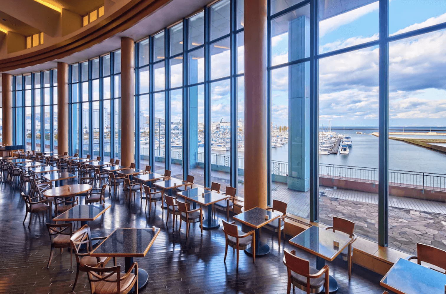 【小樽住宿】小樽公園大飯店 (Grand Park Otaru Hotel) 擁有大片落地窗的餐廳，座位整齊排列，可遠眺小樽港灣與遊艇碼頭景色。