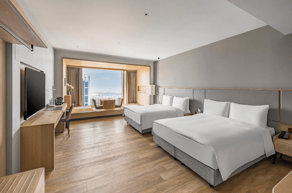 【三多商圈住宿】承億酒店 客房：溫暖木質調雙床房型，設有大片落地窗與景觀窗台座位區，可俯瞰高雄市景。