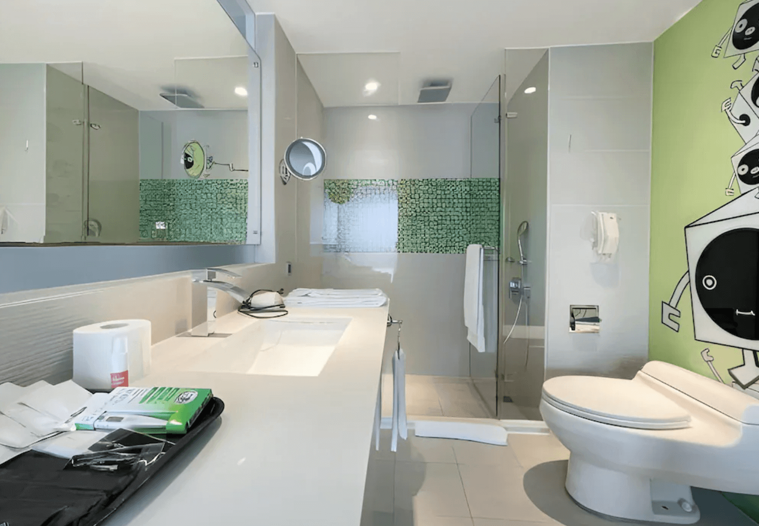 【前金住宿】承攜行旅高雄六合館 浴室，配有淋浴間、洗手檯與馬桶，綠色塗鴉牆面設計增添趣味感。