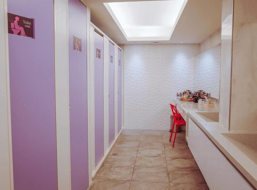 【三多商圈住宿】旅悅國際青年旅館公共衛浴空間，設有紫色隔間廁所與整潔洗手檯，並設有化妝區與座椅，方便旅客使用。