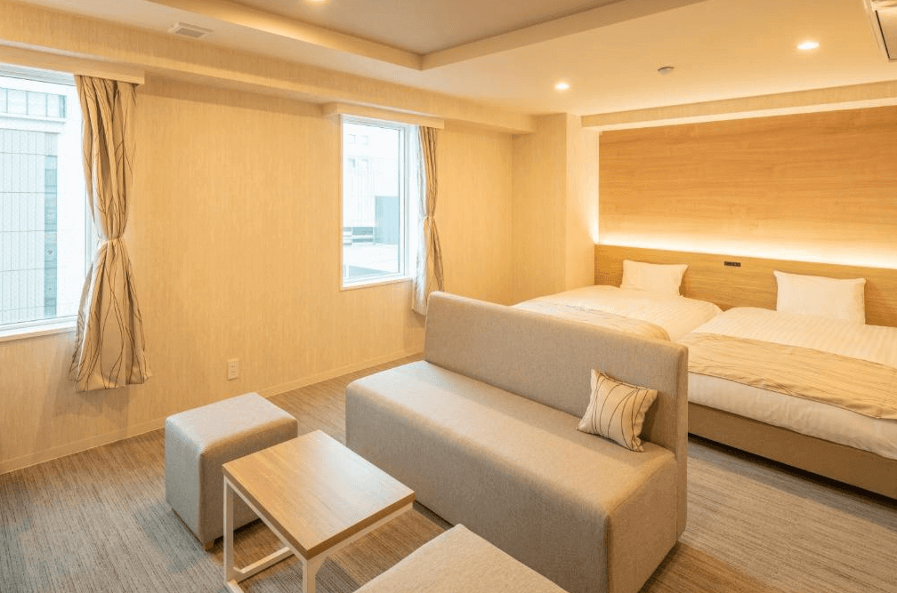 【旭川住宿】旭川HOTEL AMANEK (HOTEL AMANEK Asahikawa)客房：溫馨明亮的雙床房設計，房內設有米色沙發與小茶几，大面窗戶讓自然光灑入，氛圍舒適清新