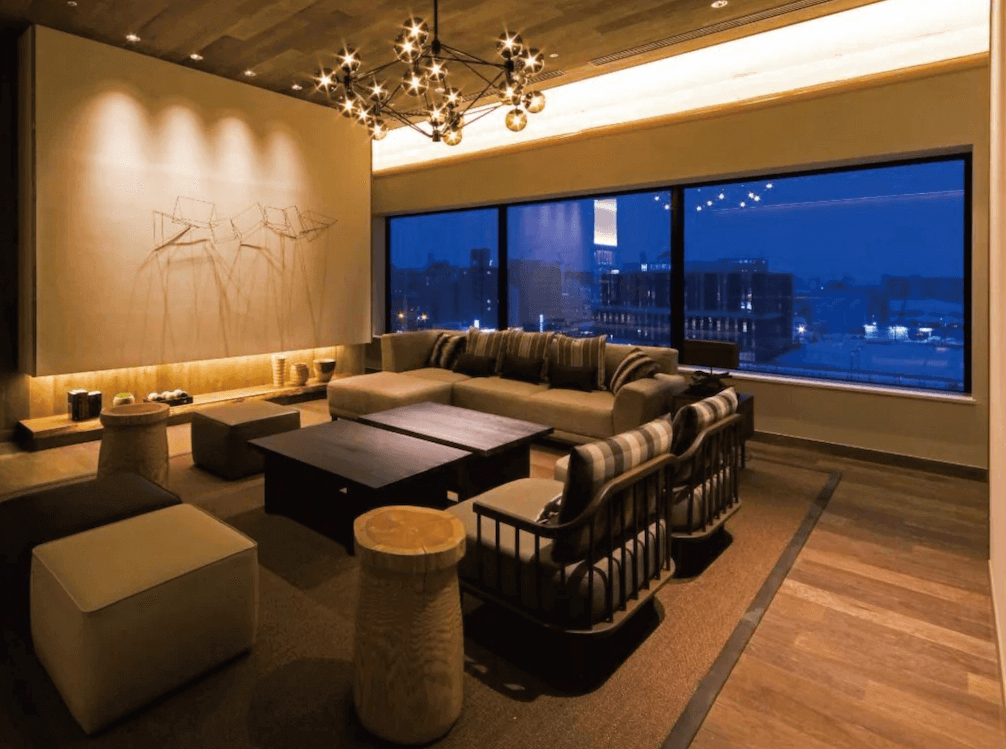 【旭川住宿】"旭川住宿精選示意圖"旭川JR飯店 (JR Inn Asahikawa) 公共休憩區，木質地板與暖色燈光，搭配舒適沙發與大面窗戶，可眺望旭川夜景，適合放鬆交流。