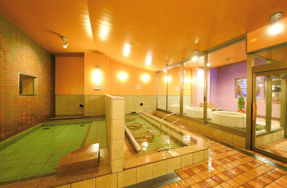 【旭川住宿】旭川WBF大飯店 (Hotel WBF Grande Asahikawa) 大浴場溫泉，溫泉池搭配岩石造景與木質天花板設計，提供放鬆舒適的泡湯體驗。