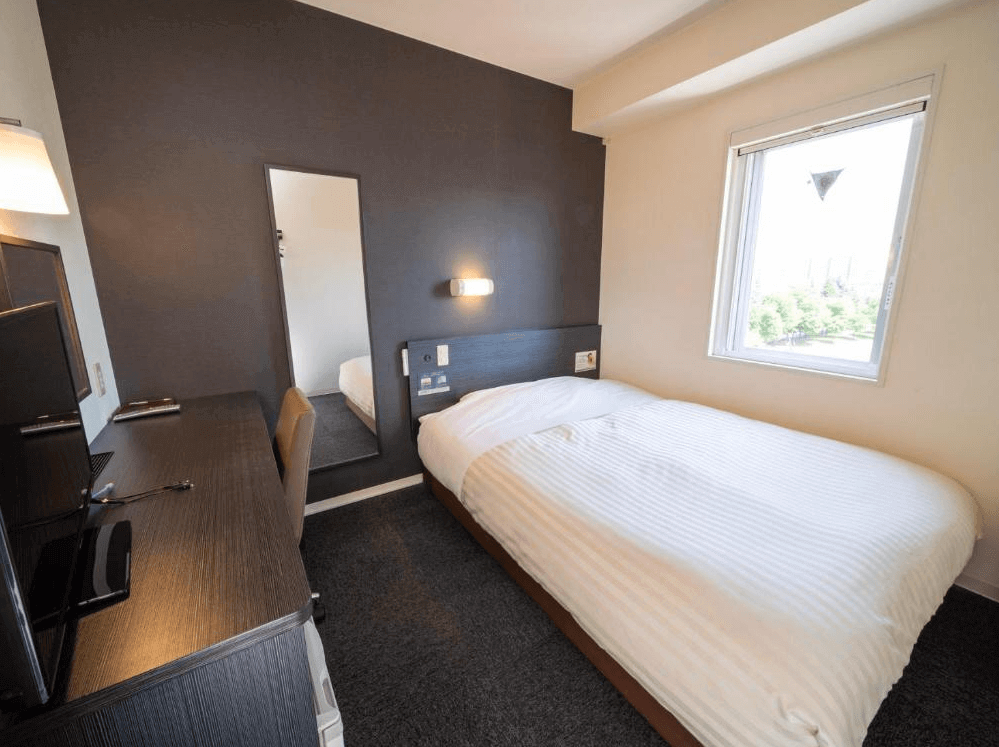 【旭川住宿】旭川超級酒店 (Super Hotel Asahikawa) 單人房，簡約設計，深色系書桌搭配大面鏡子，床鋪靠窗擺設，明亮舒適。