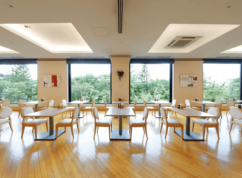 【札幌住宿】普樂美雅飯店 (Premier Hotel – TSUBAKI – Sapporo) 餐廳空間，落地窗外可欣賞綠意景觀，木質地板搭配白色座椅，營造明亮舒適的用餐氛圍。