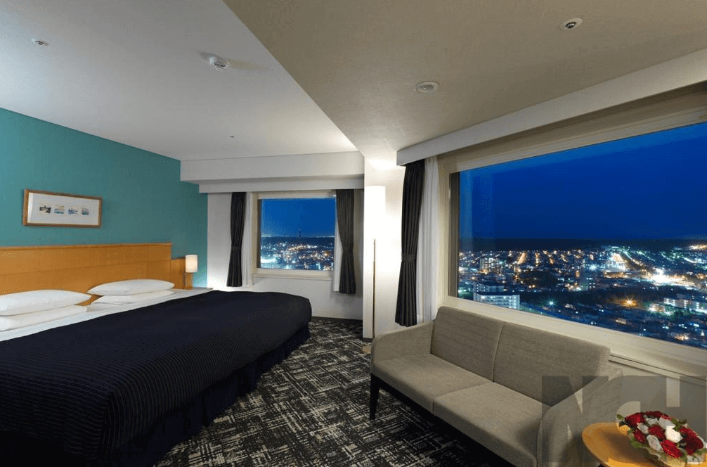 【札幌住宿】札幌Emisia飯店 景觀客房，設有大床與沙發座位，大片落地窗可俯瞰札幌夜景，氛圍典雅舒適。