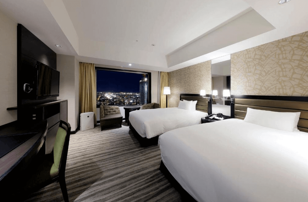 【札幌住宿】札幌JR Tower日航飯店 雙床房型，現代簡約設計，大片窗戶可俯瞰札幌夜景，房內設有辦公桌與休憩座椅。