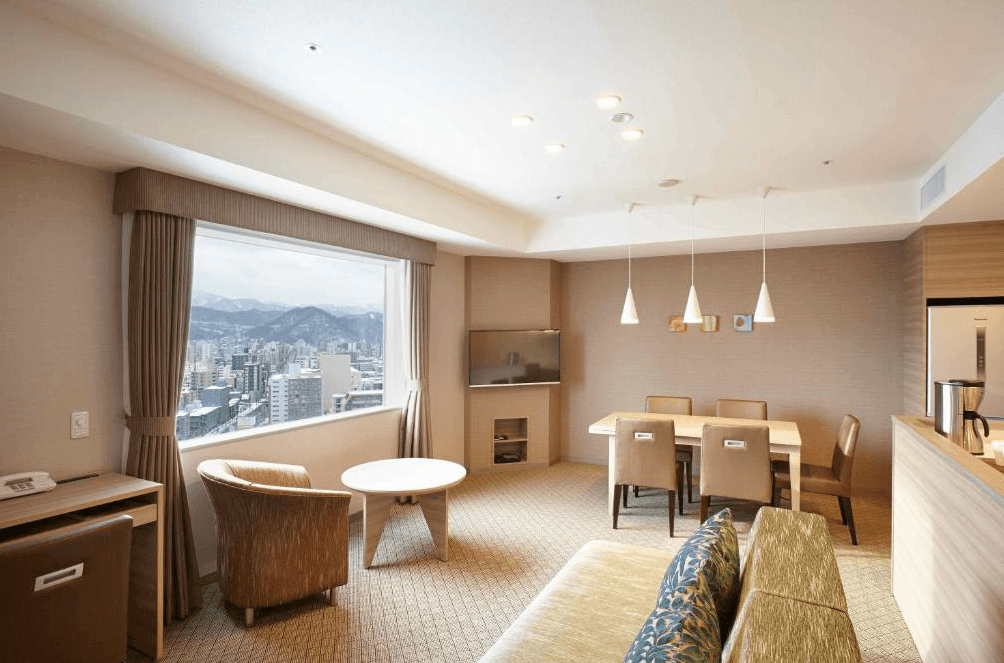 【札幌住宿】札幌東急卓越大飯店 套房空間，寬敞的客廳與餐桌區，窗外可欣賞札幌市景與山脈風光。
