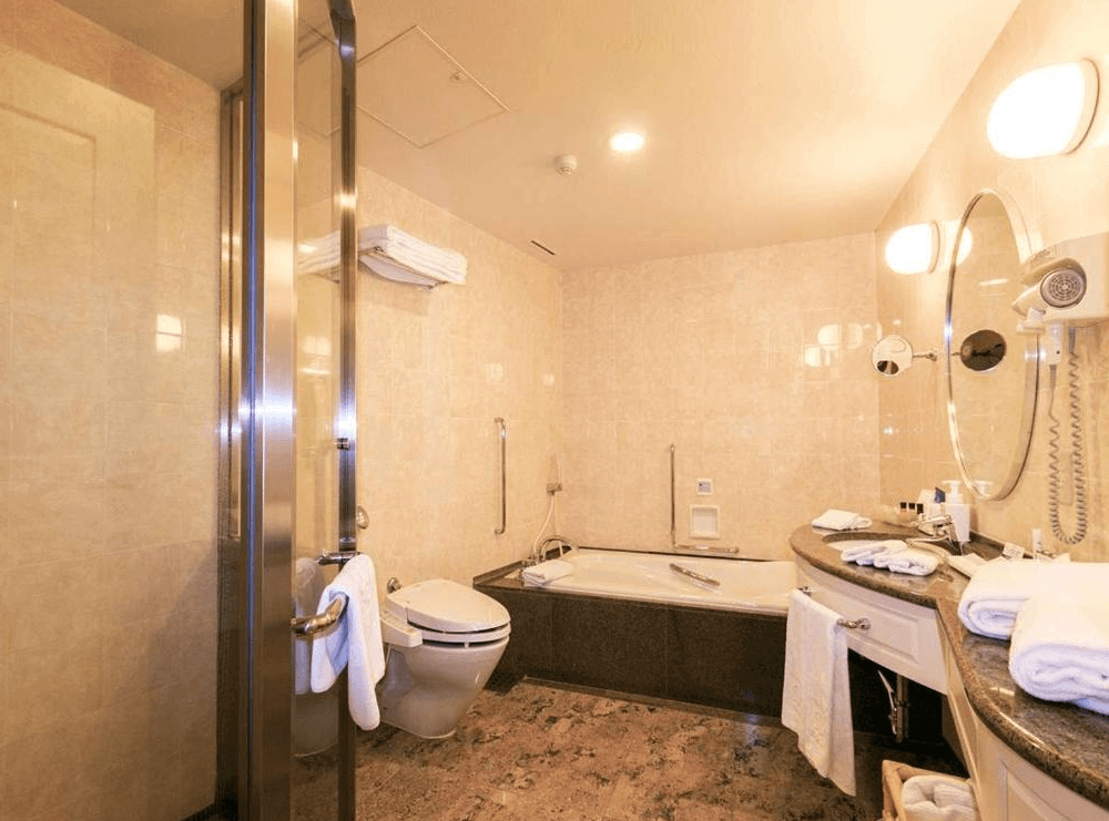 【札幌住宿】札幌王子大飯店 浴室空間，設有浴缸、乾溼分離淋浴間與齊全備品，大理石檯面與溫暖燈光營造舒適感。
