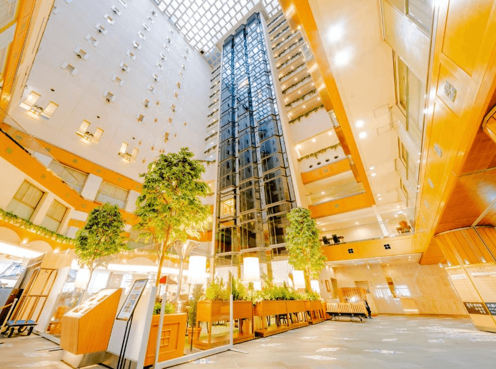 【札幌住宿】札幌豪景酒店大通公園 中庭大廳，高挑設計搭配透明天窗與電梯井，綠植與溫暖燈光營造明亮氛圍。