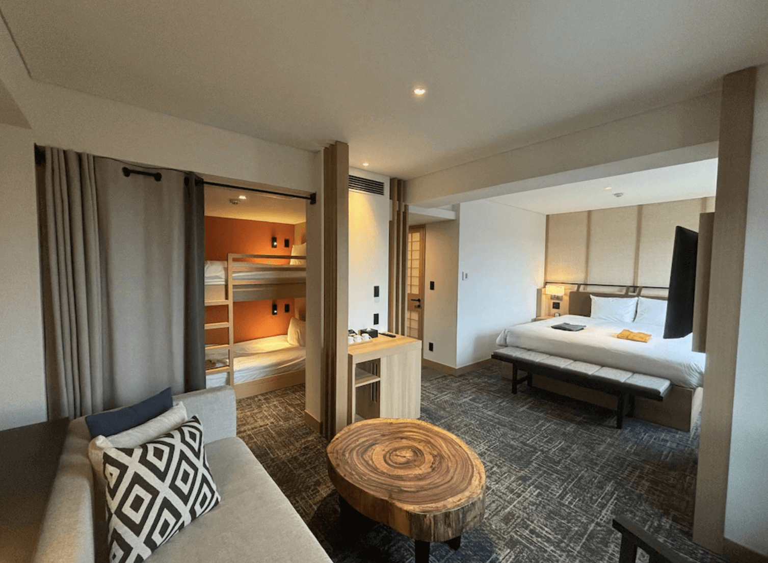 【富良野住宿】諾佐飯店家庭房：房內設有大床與上下舖，並搭配客廳休憩區與原木茶几，空間寬敞，適合親子或多人入住。