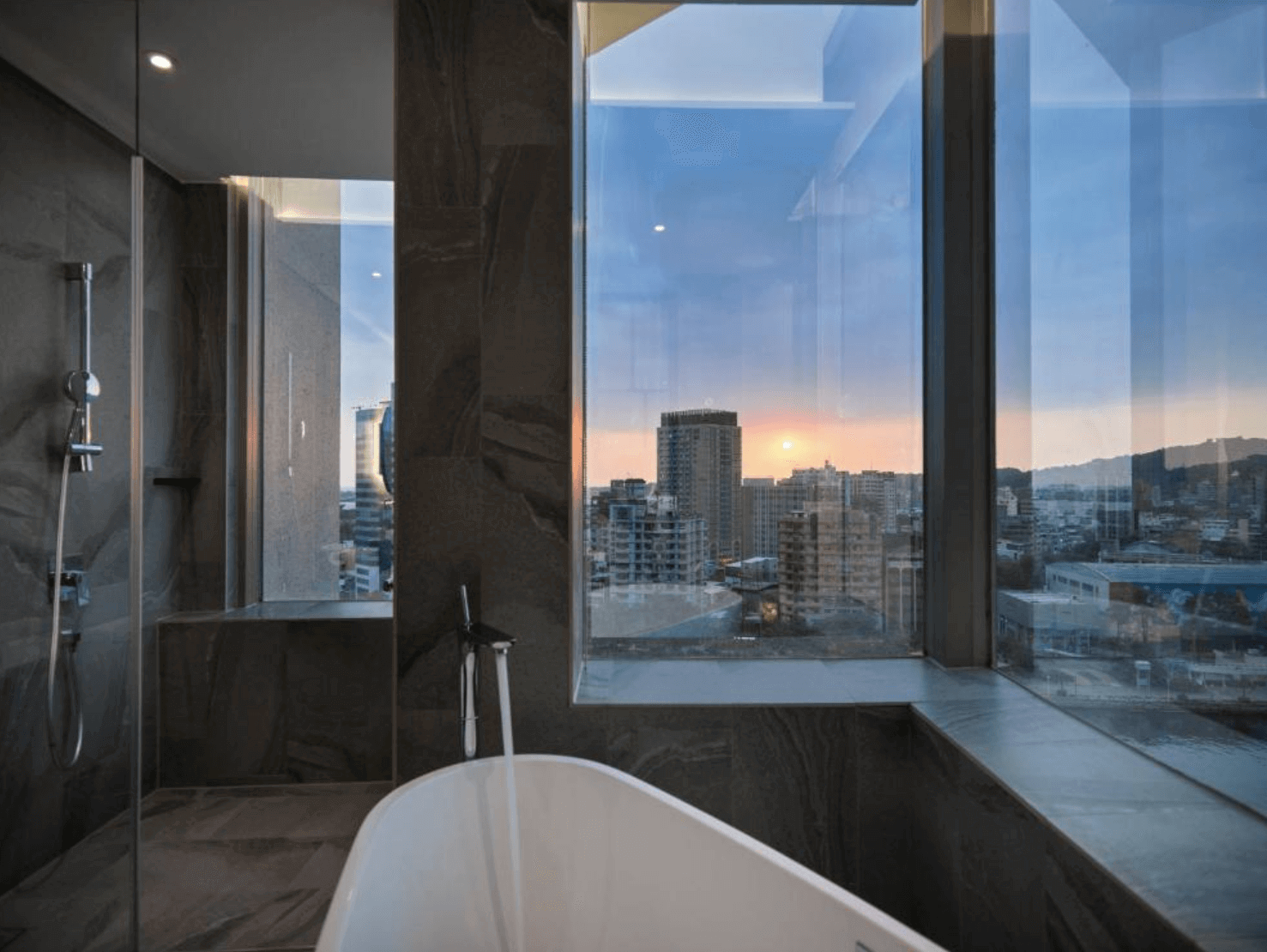 【前金住宿】鈞怡大飯店 浴室設有獨立浴缸與淋浴間，大片落地窗可眺望高雄市景與夕陽景色，氛圍高雅。