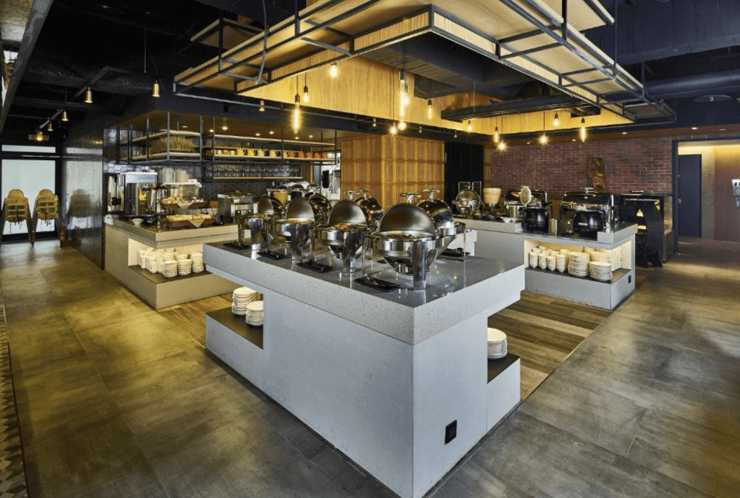 【前金住宿】鈞怡大飯店 自助早餐餐廳，現代工業風設計，中央與側邊餐台陳列多樣餐點，空間寬敞明亮。