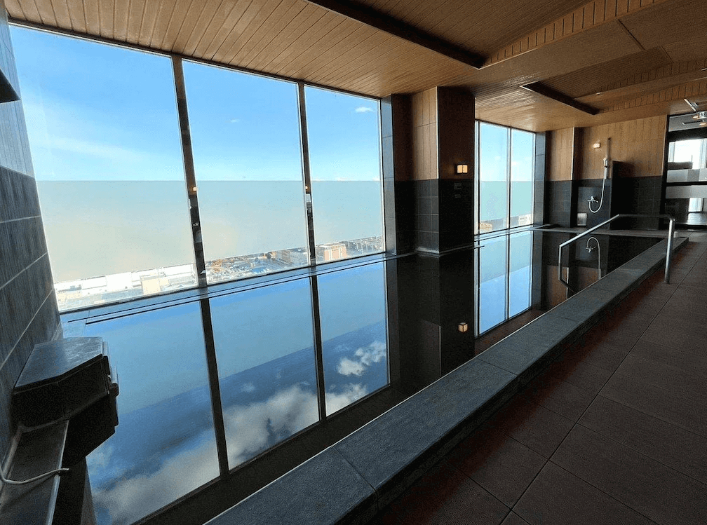 【旭川住宿】露櫻GRAND酒店旭川站前店 (Route Inn Grand Asahikawa Ekimae) 大浴場設施，設有大型溫泉浴池與落地窗，可邊泡湯邊欣賞旭川市景與天空倒影。