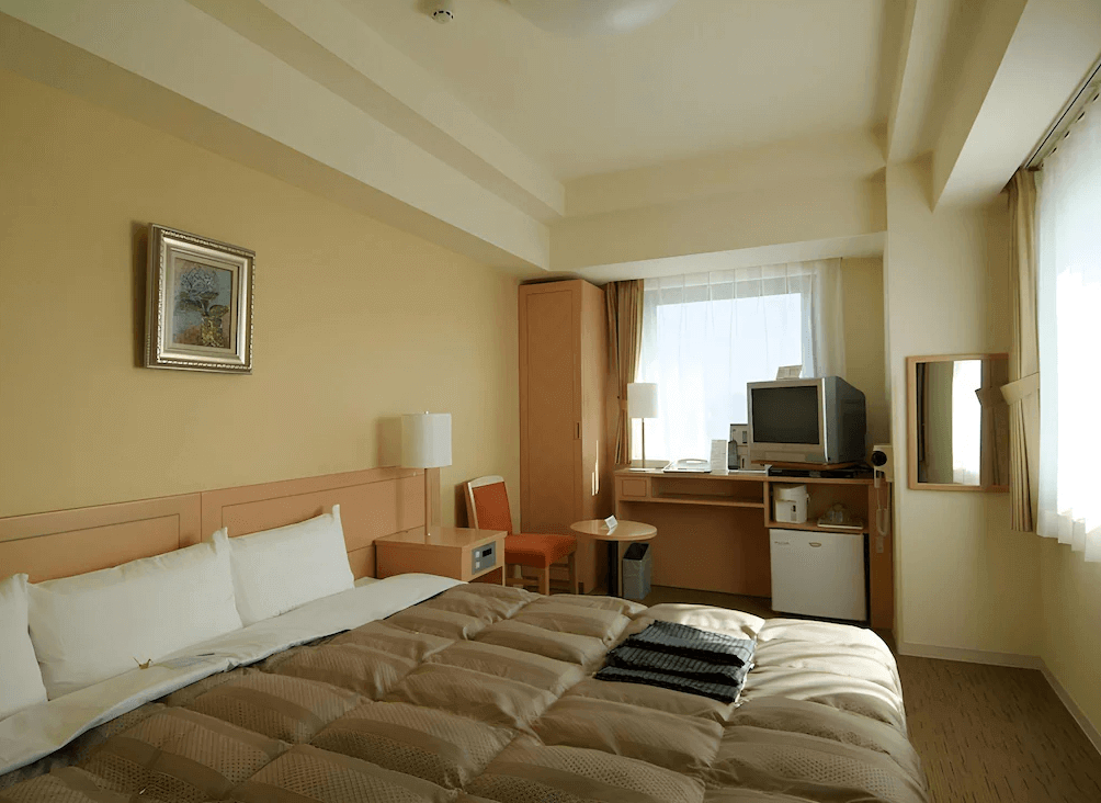 【函館住宿】露櫻GRANTIA函館站前店雙人房，米色牆面與大床搭配暖色調燈光，房內設有書桌與電視，氛圍溫馨。