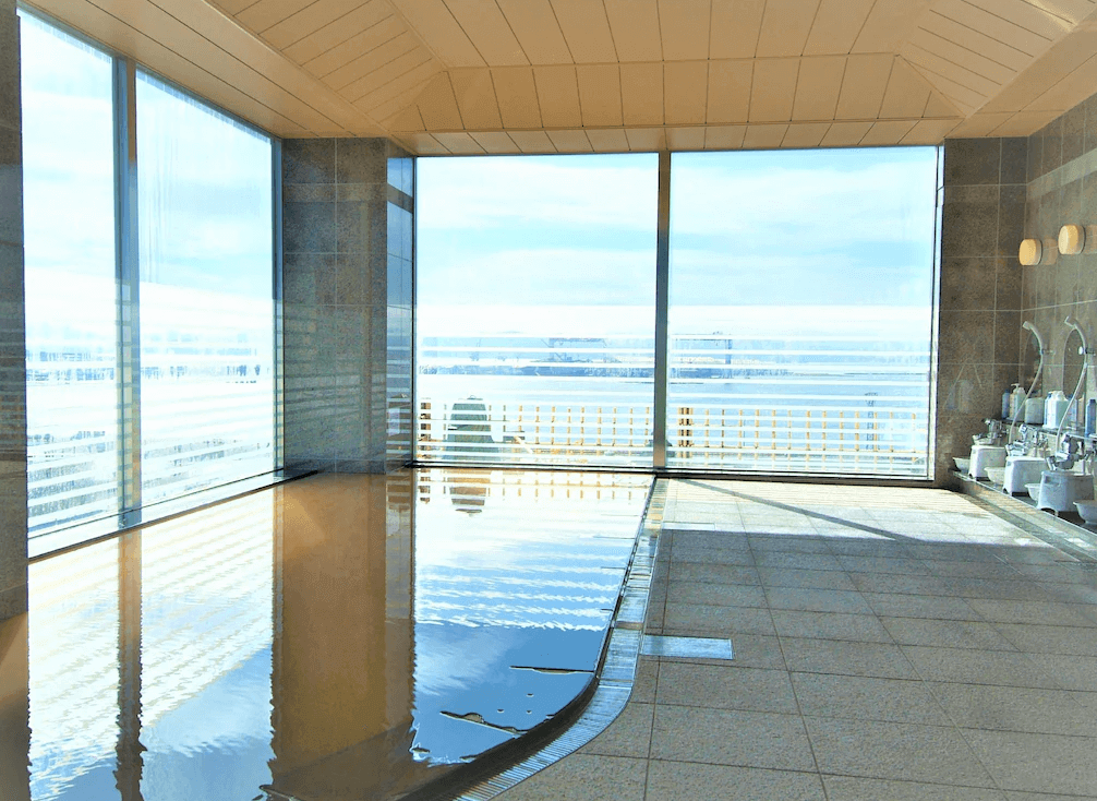 【函館住宿】露櫻GRANTIA函館站前店高樓層溫泉大浴場，大片落地窗可遠眺港口與城市景觀，浴池空間寬敞明亮。