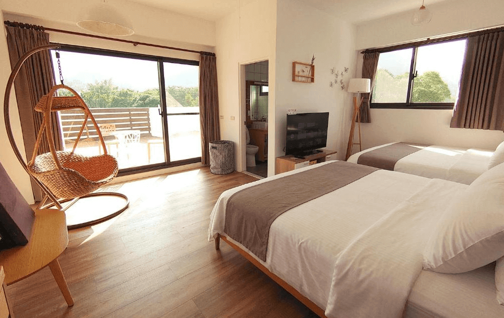 【赤柯山住宿】高寮貳陸之貳民宿房型一：溫馨明亮的雙人房，木質地板搭配大面落地窗，室內設有雙床、電視、吊椅與陽台，窗外可欣賞綠意景觀。