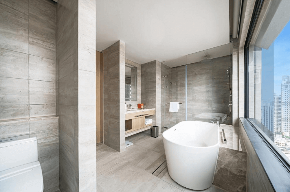 【三多商圈住宿】高雄日航酒店 浴室：大理石設計的寬敞浴室，配有獨立浴缸與乾溼分離淋浴間，窗邊可欣賞城市高樓景致。