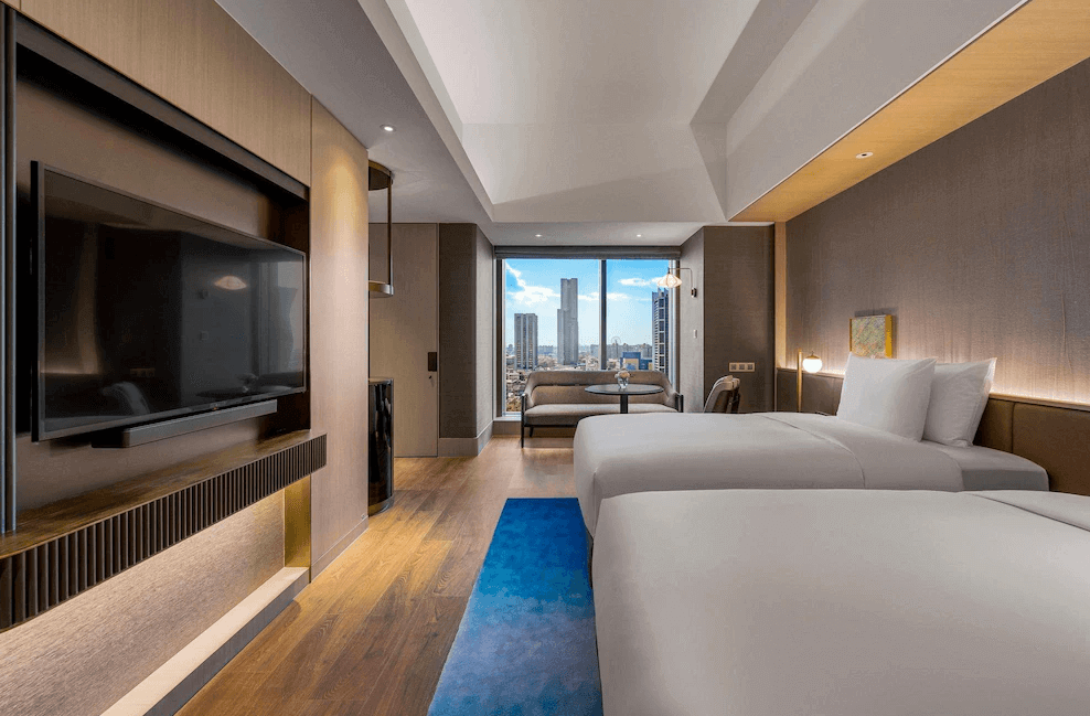 【三多商圈住宿】高雄洲際酒店現代化雙床客房，配有落地窗可眺望高雄市景，室內設計簡約雅緻，木質地板搭配藍色地毯，並設有大型液晶電視與舒適沙發區。