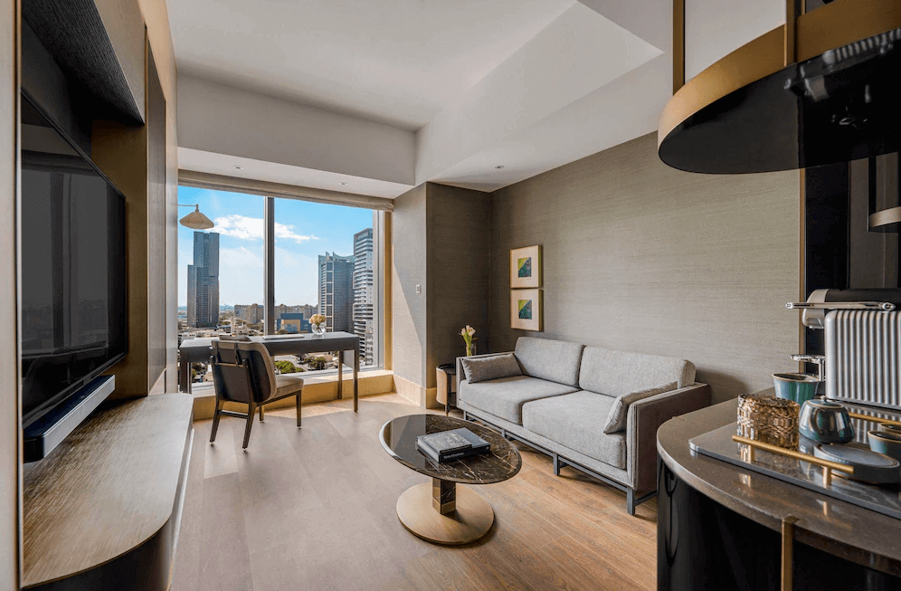 【三多商圈住宿】高雄洲際酒店套房客廳，設有灰色沙發與圓形茶几，大片落地窗可欣賞高雄摩天大樓景觀，並配備書桌與咖啡沖泡設備，空間寬敞明亮。