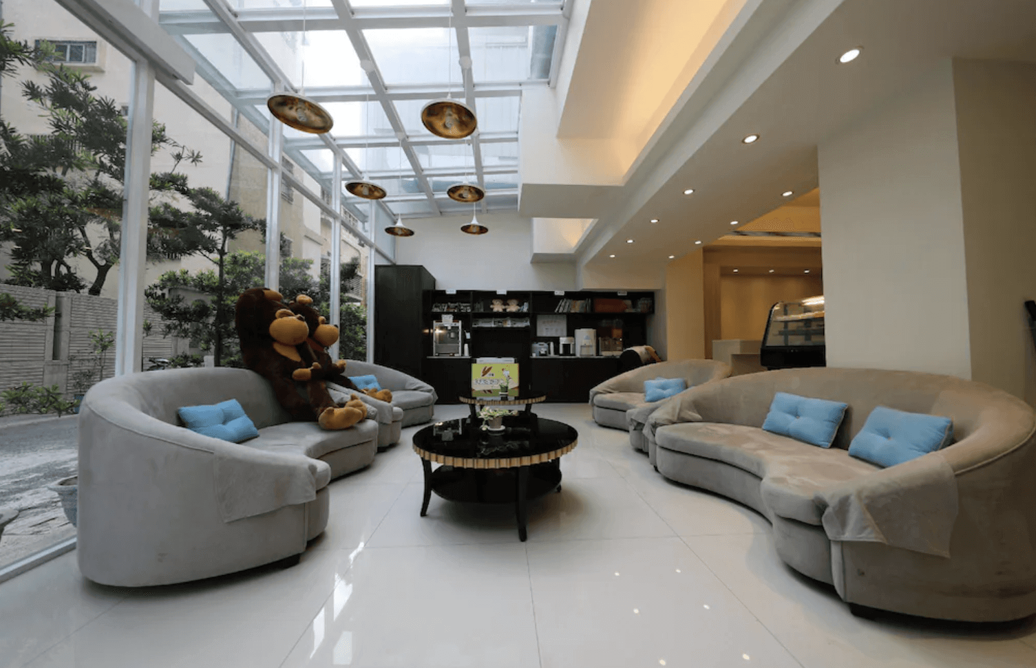 【前金住宿】高雄都會商旅 M-Hotel 大廳休憩區，採挑高玻璃屋設計，設有舒適圓形沙發與大型玩偶，氛圍明亮悠閒。