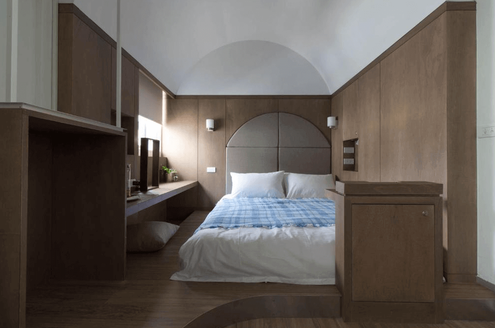 【高雄中央公園住宿】鶴宮寓客房：木質設計的大床房，搭配拱形牆面與簡約照明，營造溫暖舒適的住宿氛圍。