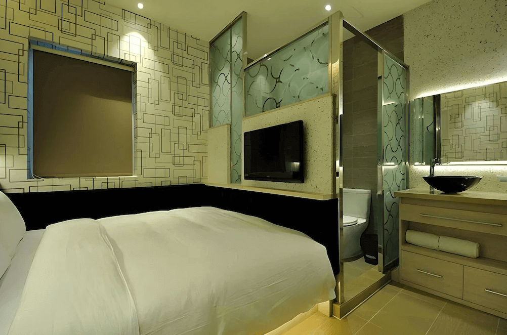 【鳳山住宿】麗馨精品商旅鳳山館 現代客房房間以幾何線條牆面設計，設有雙人床與玻璃隔間浴室，搭配電視與洗手台，營造摩登氛圍。