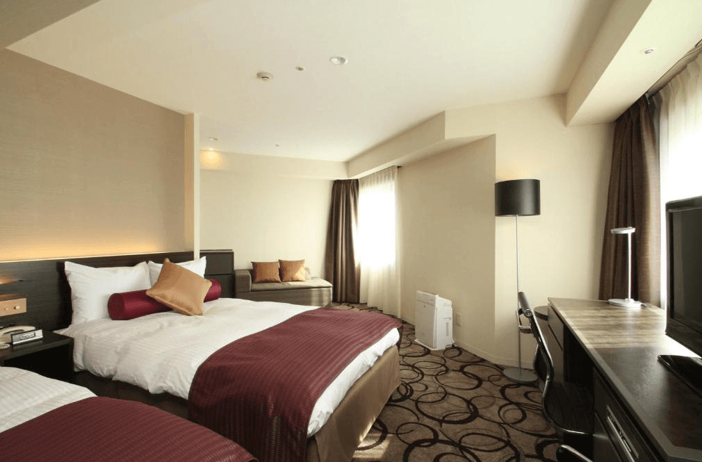 【釧路住宿】ANA皇冠假日飯店釧路客房一景，配有兩張大床與落地窗，搭配酒紅色床巾與溫暖色系裝飾，空間寬敞明亮。