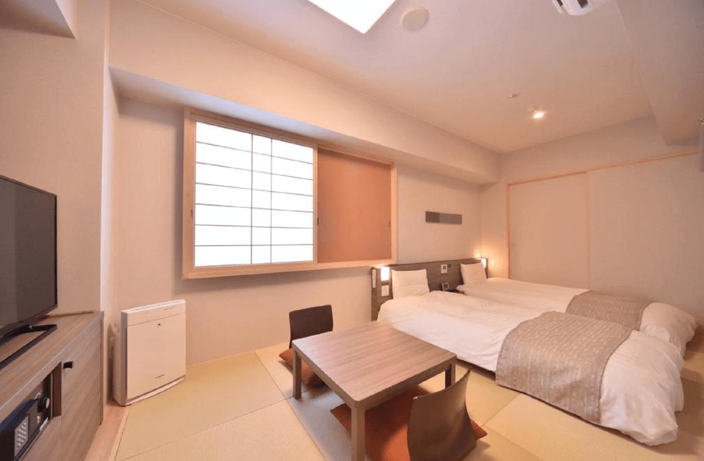 【網走住宿】「Dormy Inn 網走天然溫泉飯店」的和洋式客房，設有兩張單人床與榻榻米地板，中央擺放低矮木桌與座椅，窗邊配有日式拉門與柔和照明，整體空間明亮乾淨。