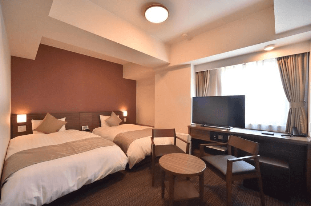 【網走住宿】「Dormy Inn 網走天然溫泉飯店」的洋式雙床房，配有暖色調牆面與柔光燈飾，兩張單人床鋪以米色被套，窗邊設有電視與木質書桌，氣氛溫馨舒適。