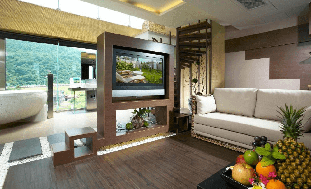 【頭城住宿】宜蘭 HOFIVILLA 和風飯店 套房客廳，設有大螢幕電視與舒適沙發，落地窗外可欣賞綠意山景與露天泡湯區。