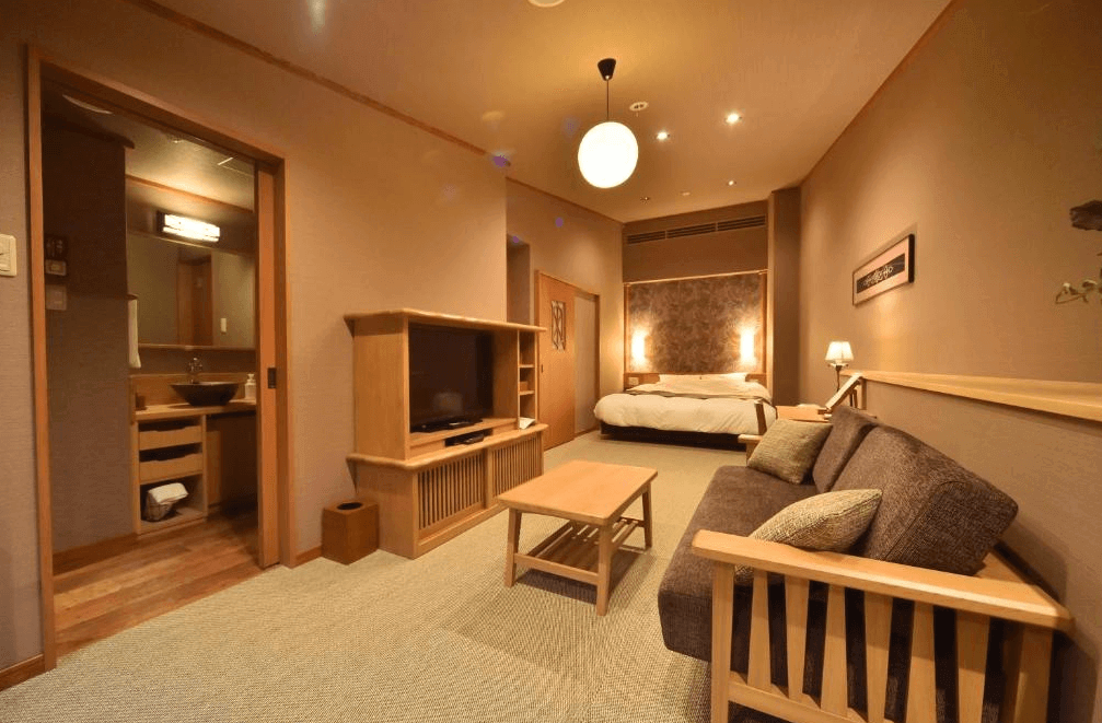 【釧路住宿】La Vista阿寒川飯店套房室內景，木質調設計營造溫暖氛圍，客廳與臥室一體成型，備有沙發、電視與雙人床，空間寬敞舒適。